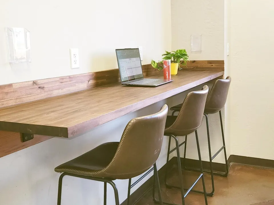 Wood work bar with leather stools, outlets, and a laptop in the lounge at The Fuge Auto Spa